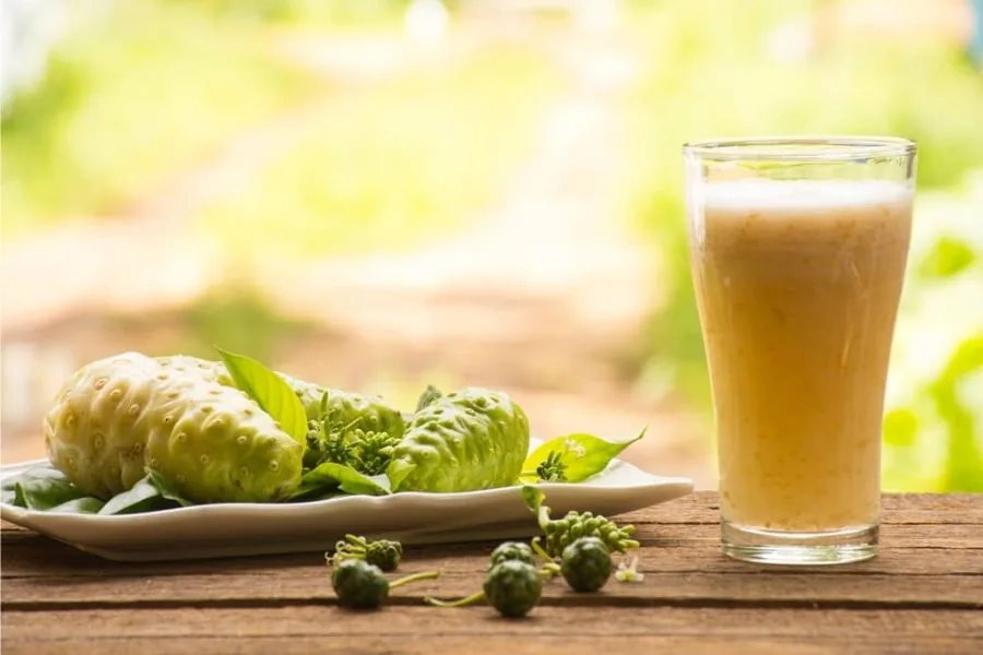 Glass of noni juice beside fresh noni fruit